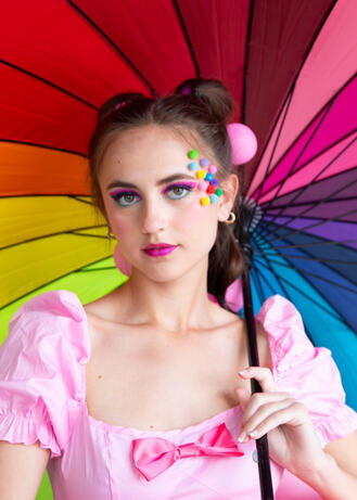 An editorial portrait of a woman with a colorful umbrella and a pink dress with a bow.