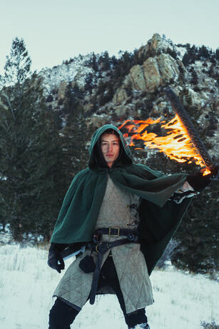 Editorial Portrait of a man in a green cloak holding a flaming sword.